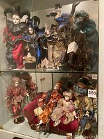 Wide view showing glass cabinet with two shelves filled with elaborately dressed Harlequin and Jester dolls including standing and seated poses.