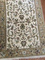 Full view of the rectangular wool rug showing the central floral pattern, cream background, and tan-beige border with floral detailing.