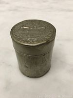 Small cylindrical metal tin viewed from the side showing overall shape and condition.