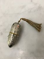 Metal travel sewing kit case with floral engravings and beige tassel, closed view