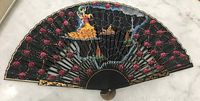 Full view of vintage handheld fan with flamenco dancer, black fabric with pink floral pattern and gold detailing.