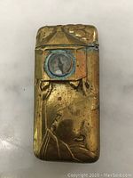 Close-up front view showing brass vesta case with embossed Japanese figure and built-in compass.