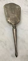 Full view of the antique hand mirror showing engraved floral pattern on back and tapered handle with patina.