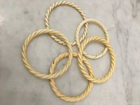 Top-down photo showing all five twisted rope design bangles laid flat on marble surface.