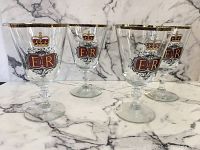 Four vintage Queen Elizabeth Silver Jubilee goblets displayed on marble surface showing front emblems with crowns and gold rim details.