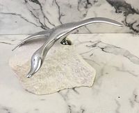 Front angled close-up of the aluminum goose sculpture mounted on white stone base showing sculptural details and surface texture.
