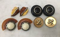 Four pairs of vintage clip-on earrings in various materials and colors on white background, showing overall appearance and design variety.