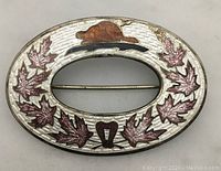 Front view of the oval sterling silver brooch with enamel Canadian beaver and maple leaf decoration.