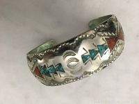 Close-up of the silver cuff bracelet showing turquoise and coral geometric inlay with hand-stamped designs.