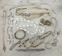 Overview of entire vintage jewelry lot showing various necklaces and bracelets laid out on a gray surface.