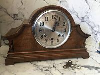 Front view of wooden antique mantle clock, showing the silver metal dial with black Arabic numerals and winding key beside it.