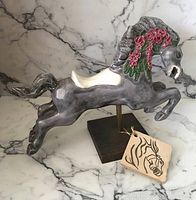 Front and side view of ceramic carousel horse figurine showing detailed gray coloring, floral mane decoration, white saddle, and wooden base.