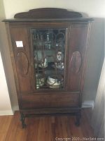 Front view of the dark wooden hutch showing the original glass central door with decorative wooden panels inside, side wooden doors, drawer, and carved legs.
