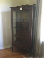 Front view of oak curio cabinet showing carved crest and glass door
