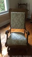 Front view of antique oak rocking chair showing carved wooden frame and floral upholstered seat and back.