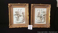 Pair of Meissen bisque plaques with ornate gold frames on black background. Both show relief scenes of a man playing mandolin and woman sitting next to him.