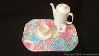 Photo showing vintage Johnson Brothers Athena coffee pot with one cup and saucer placed on a colorful quilted floral placemat on a black background.