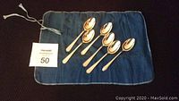 6 International sterling silver spoons laid on blue cloth, showing front sides.