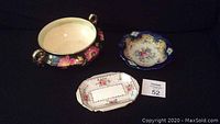 Three assorted vintage decorative china dishes on dark background, including floral Royal Albert Petit Point rectangular dish, hand painted floral shallow bowl with gold accents, and deep blue shallow floral dish.