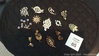 Full lot arrangement showing all 11 rhinestone brooches and 2 pairs of Continental earrings on a dark quilted surface.
