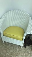 Front angle view of white wicker chair with yellow cushion against wall
