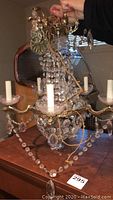 Chandelier held by hand showing entire fixture from above: brass frame, central glass bowl and cascading crystal beads.