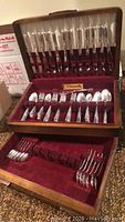 Wooden two-tier presentation box with red velvet lining showing the silver plate flatware for twelve persons including knives, forks, and spoons.