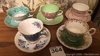 Five assorted vintage tea cups and saucers with unique floral and gold trim patterns displayed on wooden surface.