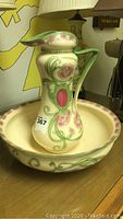 Front view of cream ceramic pitcher with pink and green floral decoration atop matching bowl