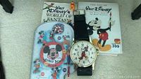 Overview photo showing two Disney books, oversized Mickey Mouse wall clock, and a vintage Mickey Mouse pinball game.