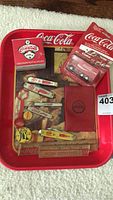 Photo of entire lot showing Coca Cola advertising tray, toy truck in packaging, various bottle openers, and pin-back buttons