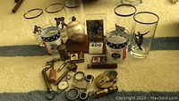 Wide view of lot showing two commemorative glasses, baseball in holder, multiple brass objects including padlock, whistle, razor, and other small collectibles.