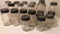 Top view of 18 vintage glass canning jars with metal lids on a white surface.