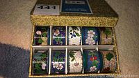 Top view of ten cloisonné napkin rings arranged inside decorative box showing various floral patterns.