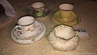 Set of four tea cups and saucers arranged on carpet showcasing different floral patterns and shapes.