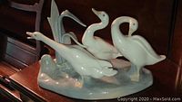 Front angle view of Lladro porcelain geese group figurine showing three white geese with water base and reeds.