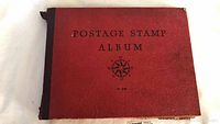 Front cover of red hardcover album embossed “POSTAGE STAMP ALBUM No. 308” and compass rose design