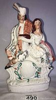 Front view of the hand painted Staffordshire flatback figurine depicting a seated man playing bagpipes and a woman in period costume.