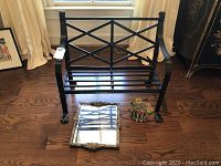 Full view of black wrought iron bench with claw feet, antique mirror, and floral cast iron door stop placed on floor in front of window.
