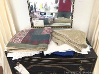 Stack of folded assorted linens including silk and lace tablecloths on a dresser