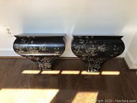 Pair of black curved wood wall shelves side-by-side showing floral painted surface and curved profile.