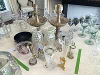 Overview of candle holders, glass chimneys, mosaic glass bud vases, green stemmed wine glasses, small candelabra and additional glassware on table