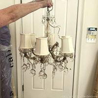 Image showing the chandelier held up by a person, displaying fabric shades, crystals, and curved metal arms.