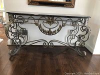 Front view of custom sofa table showing black marble top with crack and decorative iron base with leaf motifs and scrollwork.