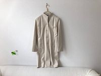 Full length view of cream leather jacket hanging on gold hanger against white wall and beige couch