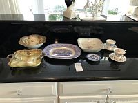 Overview of the lot including various vintage china cups, saucers, bowls, and plates on a black counter.