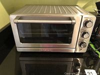Front view of Cuisinart toaster oven showing stainless steel body, glass door, handle, and control knobs on the right side.