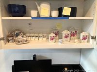 Kitchen shelf with various ceramic kitchen storage items and canisters, showing different styles including French ceramic canisters with floral motifs and smaller labeled canisters