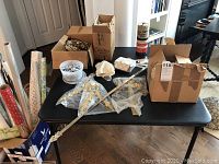 Wide view of the table with multiple boxes containing assorted crystal pendants, prisms, lamp parts, and fabric plant holders scattered on top and inside boxes.