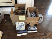 Two open boxes containing square and rectangular ceramic tiles in blue and white, with some tiles displayed in front.